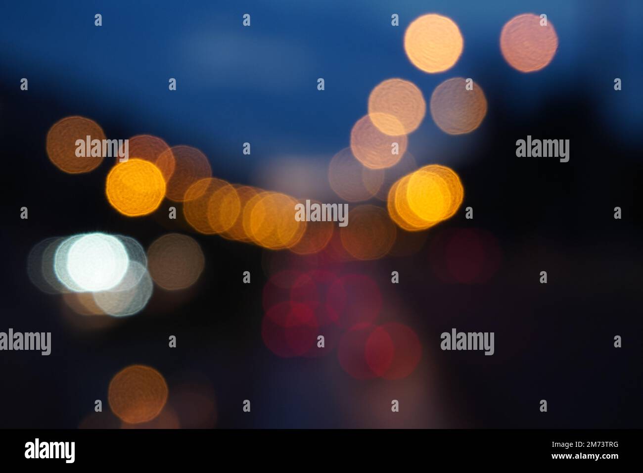 Bokeh sfondo astratto del traffico stradale cittadino sfocato con luci per auto e lampioni di notte. Colori luminosi puntini su sfondo blu scuro. Foto Stock