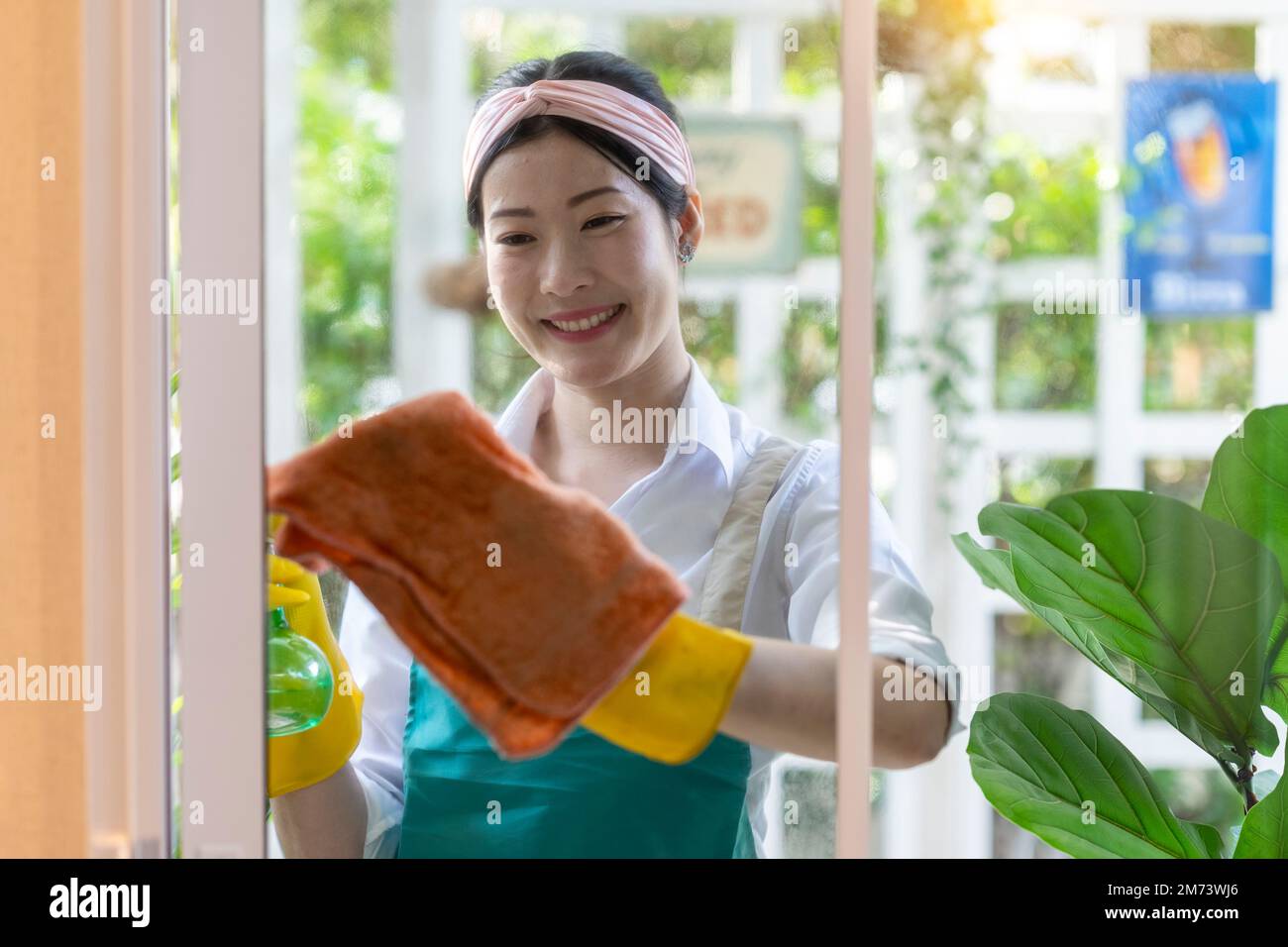 Felice giovane donna asiatica finestra di pulizia a casa, casa di pulizia o concetto di lavori domestici. Foto Stock