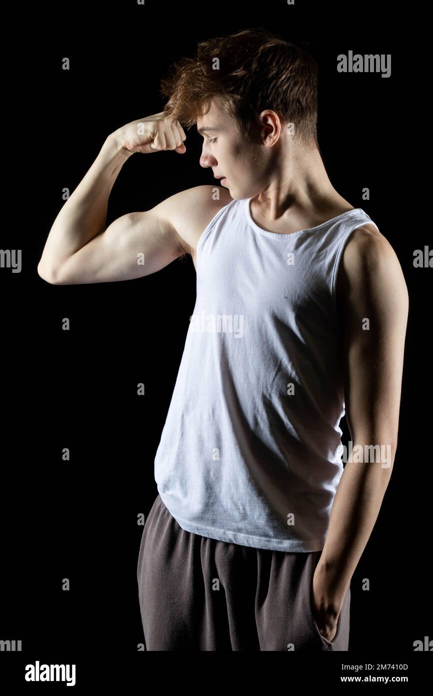 Un ragazzo di 17 anni che indossa una canotta bianca che flette i muscoli del braccio Foto Stock