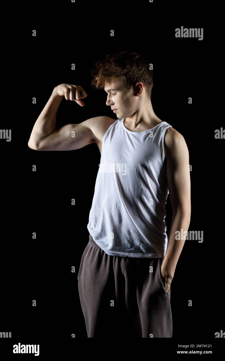Un ragazzo di 17 anni che indossa una canotta bianca che flette i muscoli del braccio Foto Stock