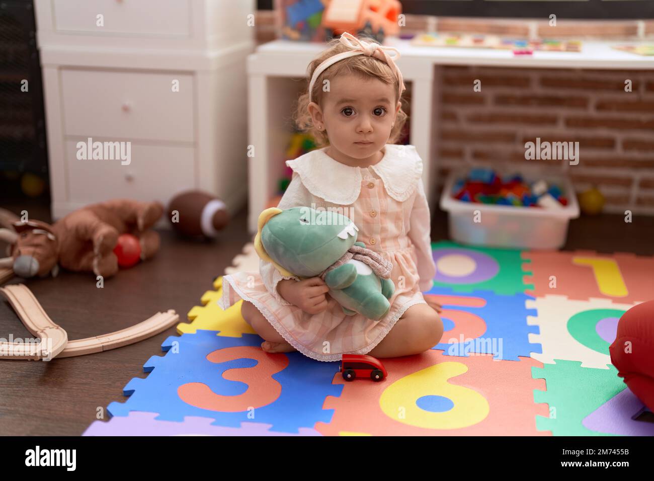 Adorabile ragazza caucasica che gioca con bambola seduta sul pavimento all'asilo Foto Stock