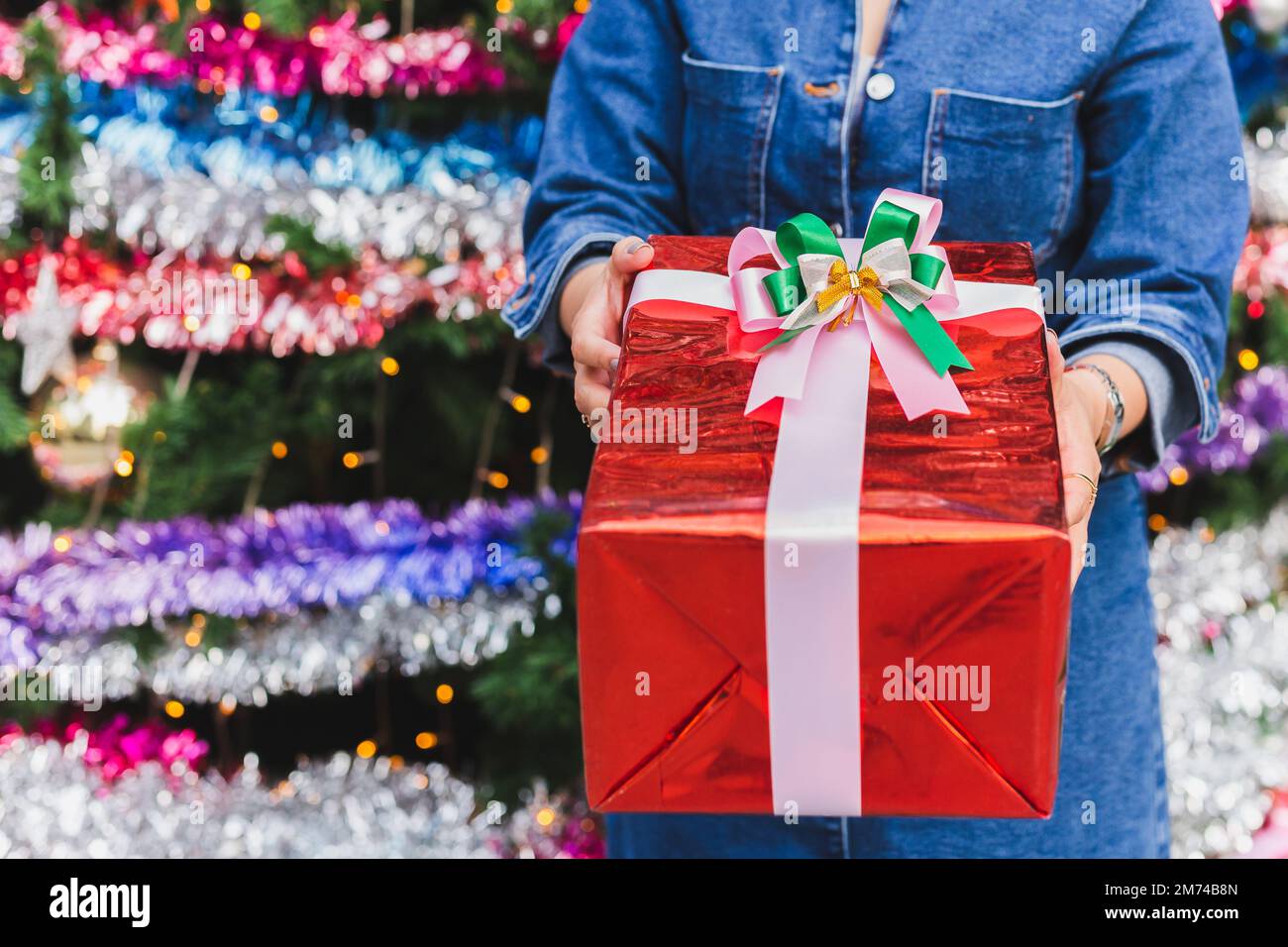 Donna che tiene presente in una scatola rossa sullo sfondo dell'albero di Natale. Foto Stock