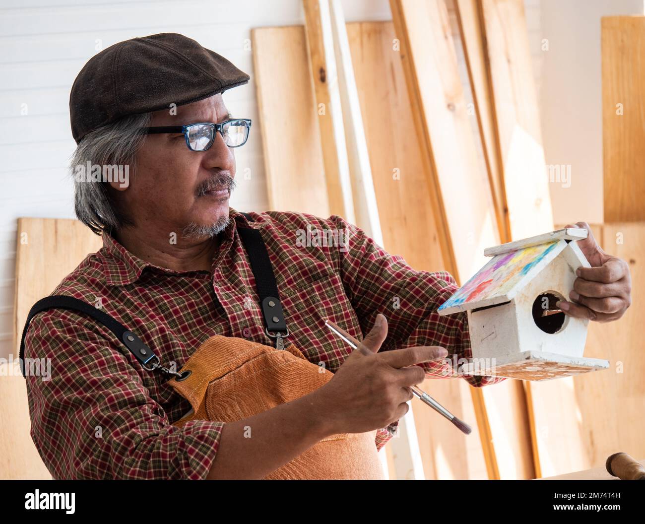 L'uomo anziano asiatico felice sta godendo il suo hobby da dipingere diligentemente birdhouses nel laboratorio. Foto Stock