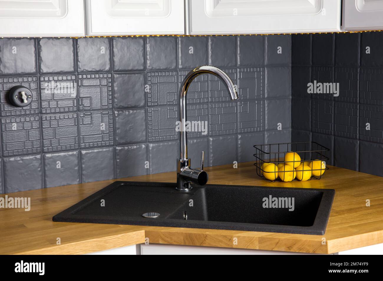 Vista ravvicinata della nuova cucina moderna, con banco in legno massello di macellaio e quercia, con lavabo in granito nero rettangolare, parete in mattonelle di colore grigio ridipinta. Foto Stock