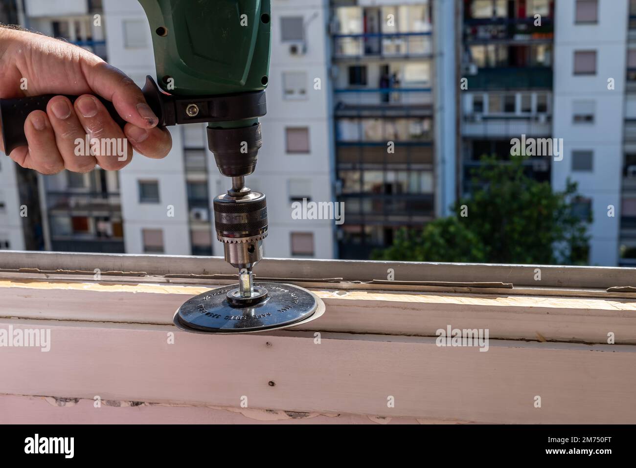 Levigare un vecchio telaio della finestra durante i lavori di ristrutturazione con un edificio di appartamenti sullo sfondo Foto Stock