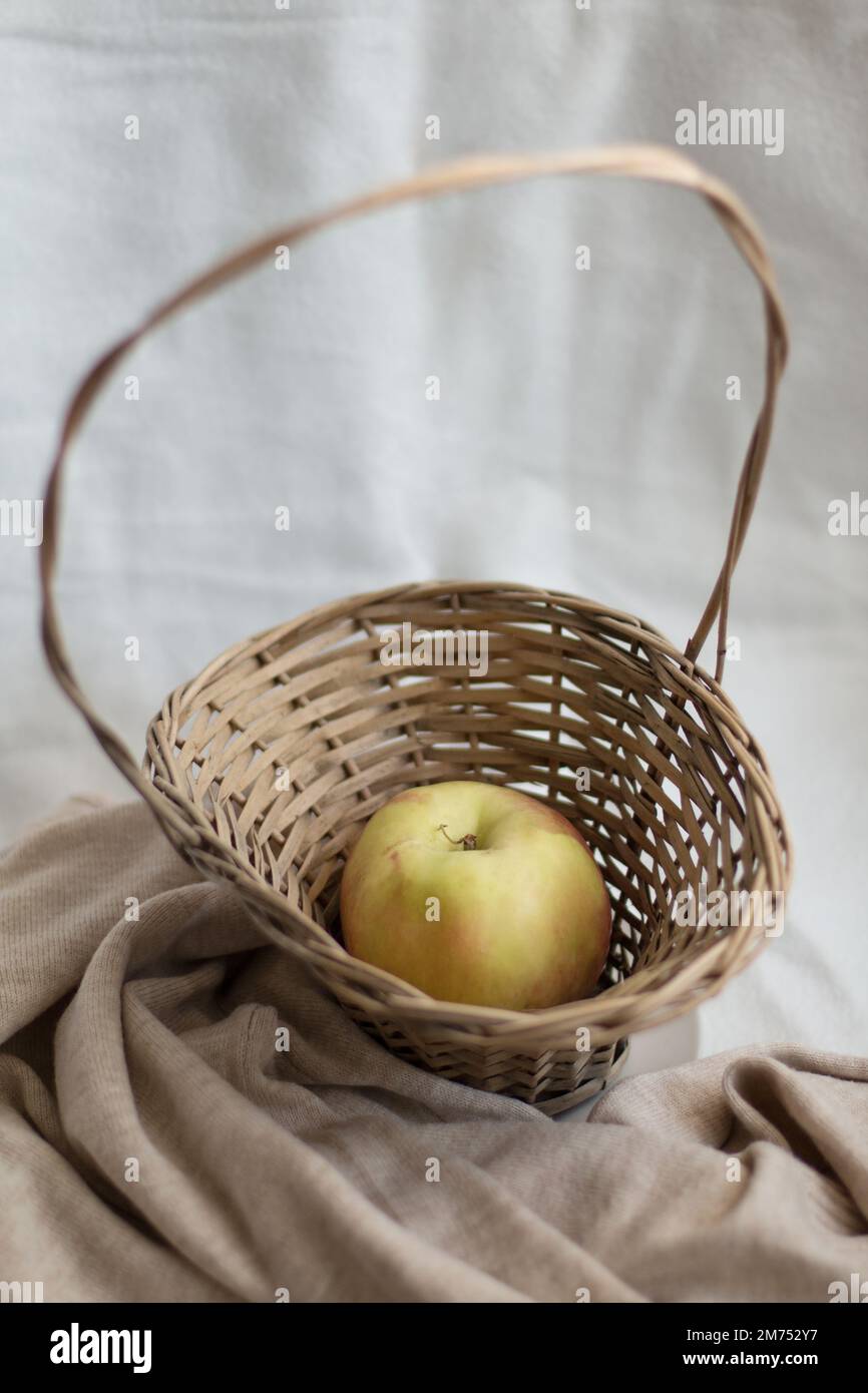 Composizione intima di vita morta di una mela in un cestino di vimini. Concetto di vita sano e semplice. Foto Stock