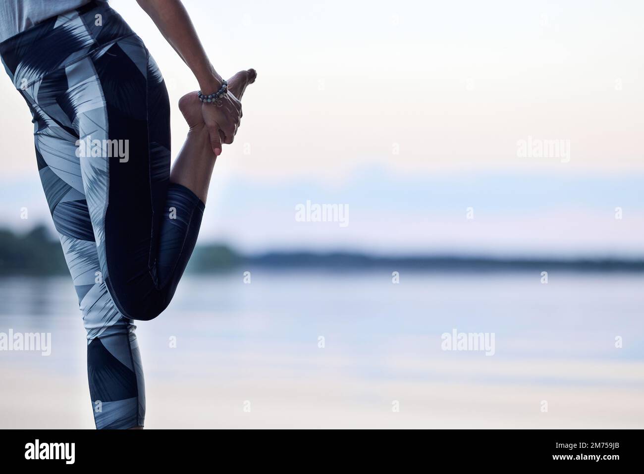 Una donna pratica lo yoga e l'equilibrio su un piede sul molo vicino al fiume in natura. Foto Stock