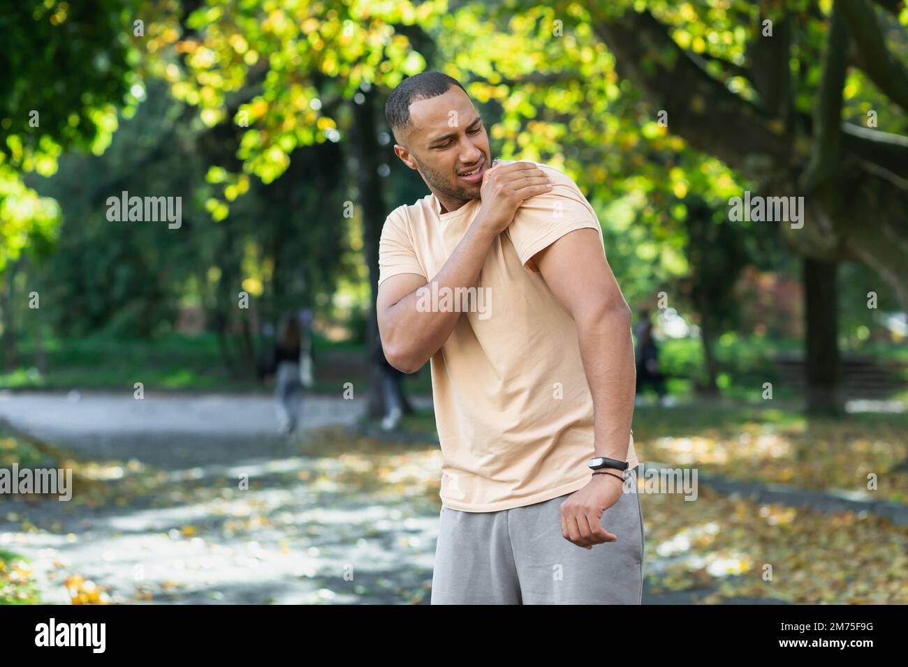 Un uomo ferì la spalla durante una lezione di fitness, un uomo afroamericano ferì se stesso mentre faceva jogging nel parco, allungò il braccio e massaggiò i muscoli irritati. Foto Stock Un uomo ferì la spalla durante una lezione di fitness, un uomo afroamericano ferì se stesso mentre faceva jogging nel parco, allungò il braccio e massaggiò i muscoli irritati. Foto Stock