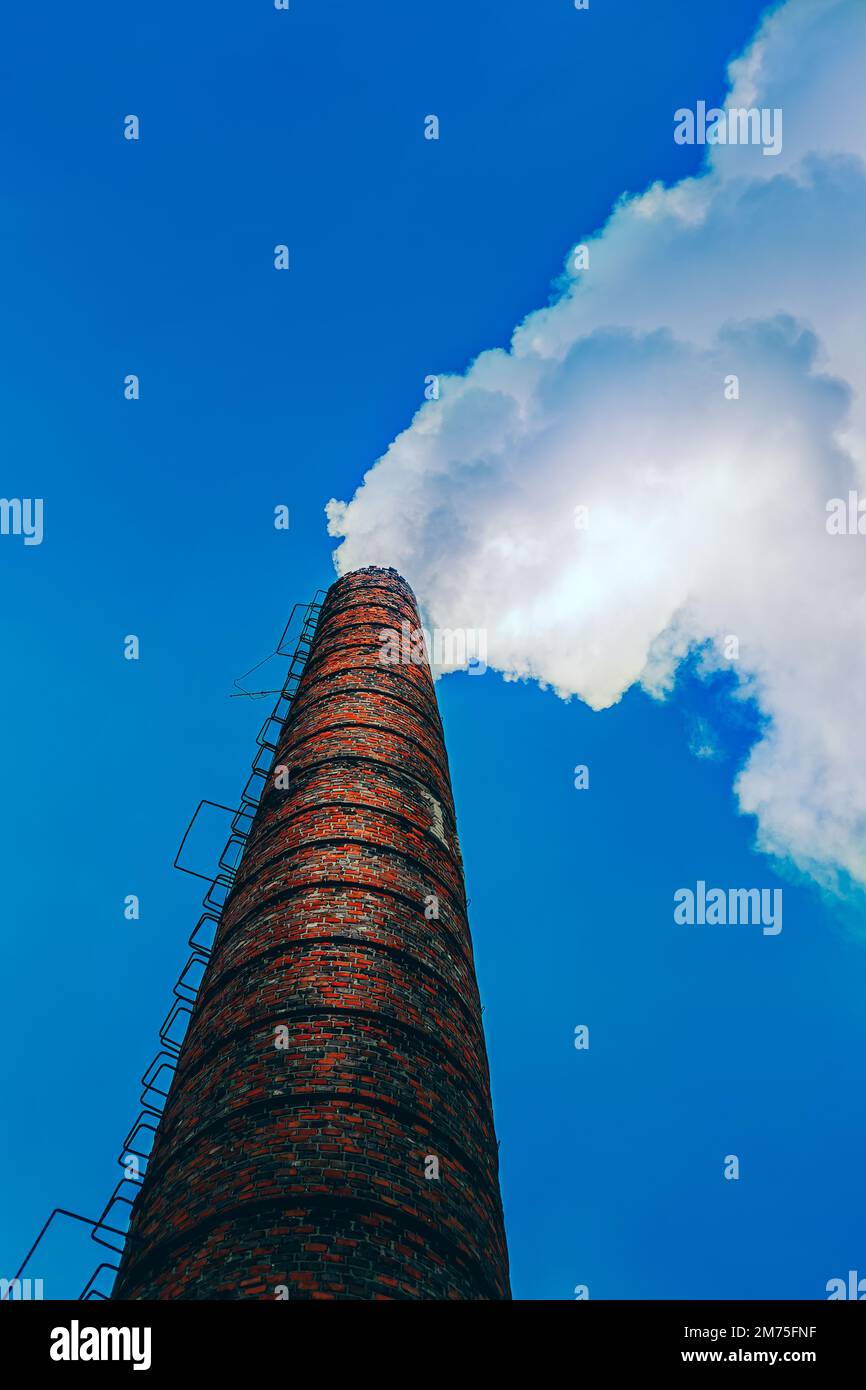 un vecchio camino di mattoni rossi contro il cielo da cui proviene il fumo Foto Stock