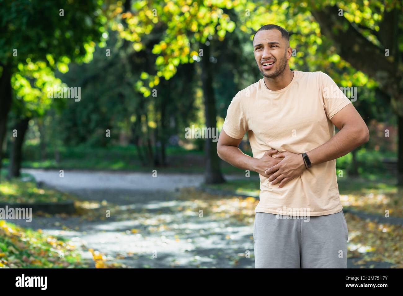 Atleta latino-americana ha un grave dolore allo stomaco, l'uomo che tiene la mano a fianco dello stomaco dopo aver fatto esercizio fisico e fitness nel parco esterno. Foto Stock