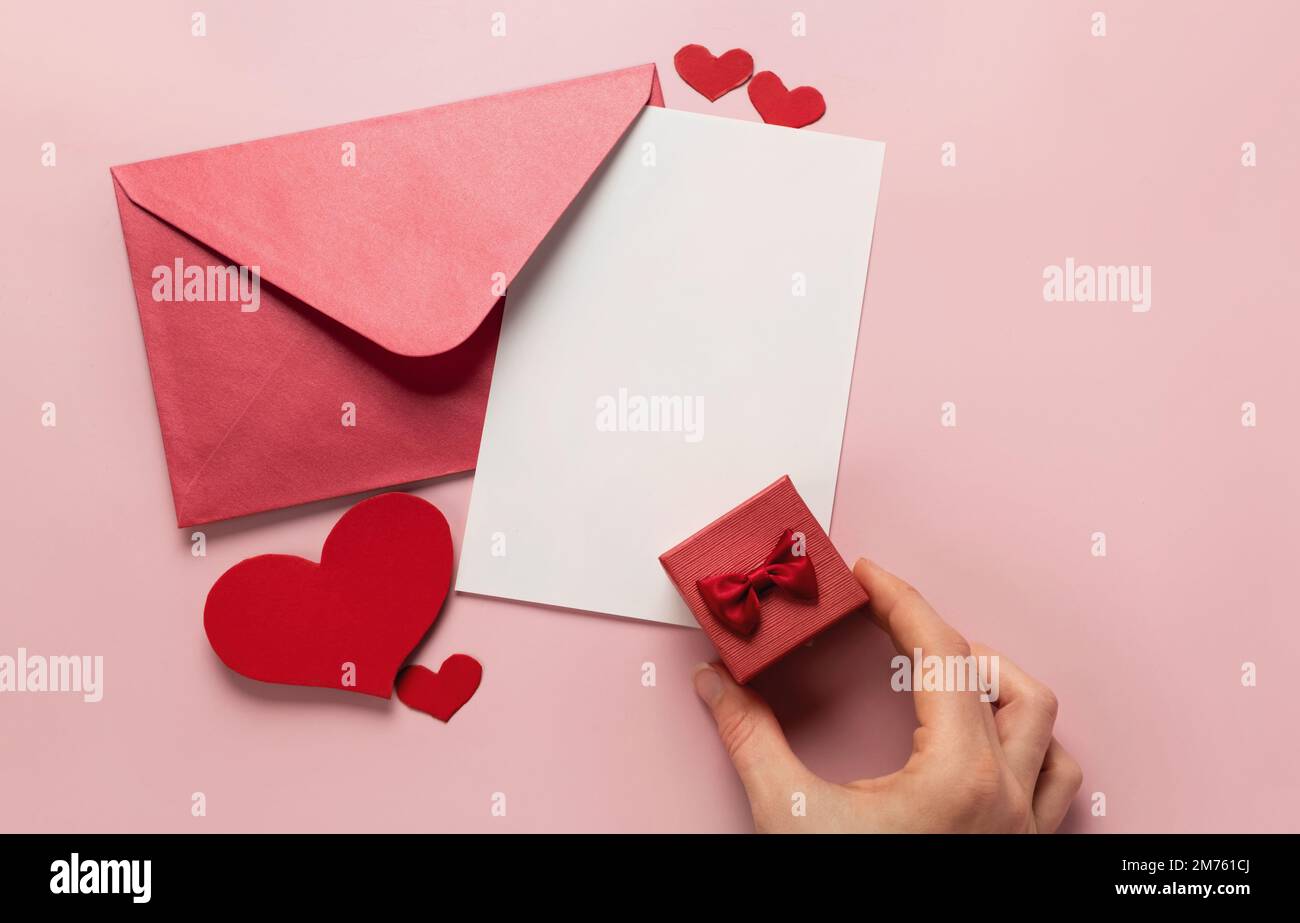 Regalo di San Valentino in scatola, lettera e busta con spazio copia su sfondo rosa. Anello per la proposta di matrimonio, piatto. Invito di nozze Foto Stock