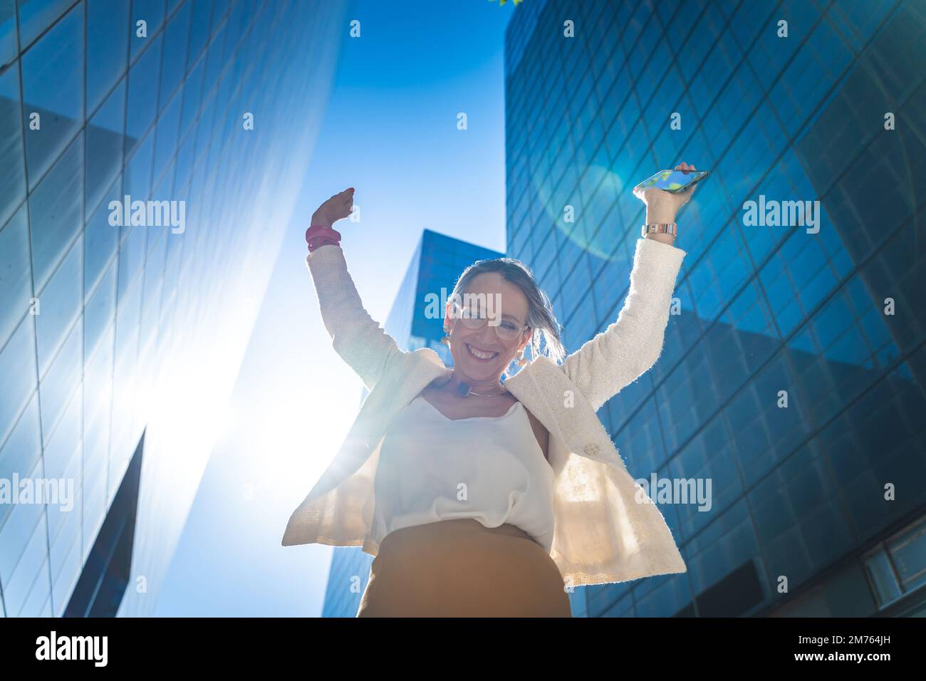 Donna d'affari felice che celebra le buone notizie davanti agli edifici di affari. Foto Stock