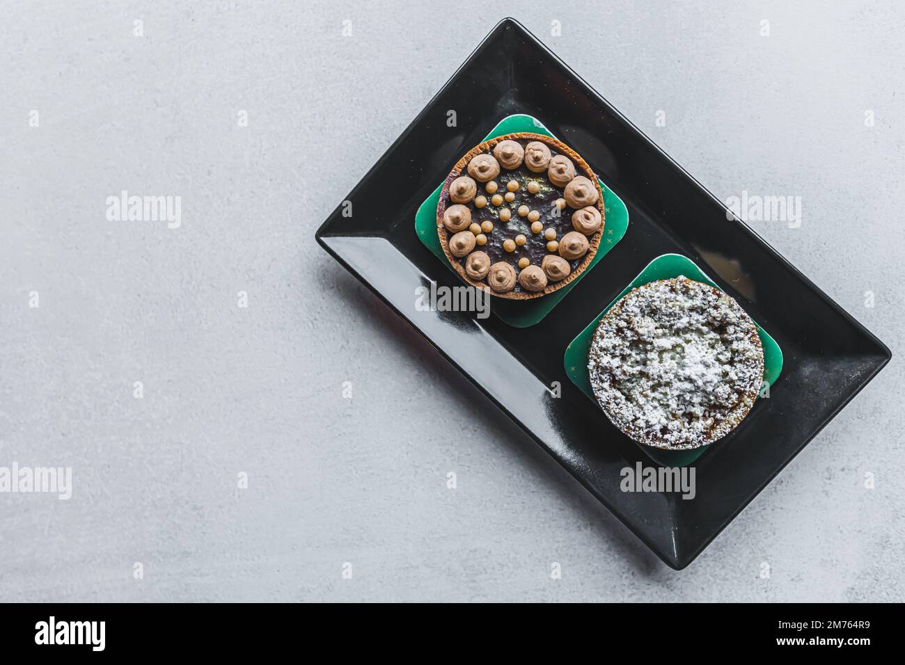 Due gustose crostate giacenti sul piatto nero su un tavolo grigio. Pasticceria d'arte. Vista ad angolo alto. Spazio di copia. Foto di alta qualità Foto Stock