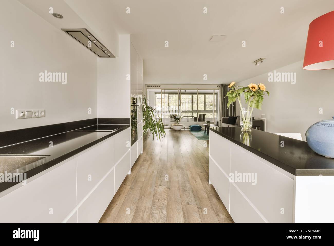 una cucina moderna con armadi bianchi e ripiani neri al centro della stanza è una lampada a sospensione arancione Foto Stock