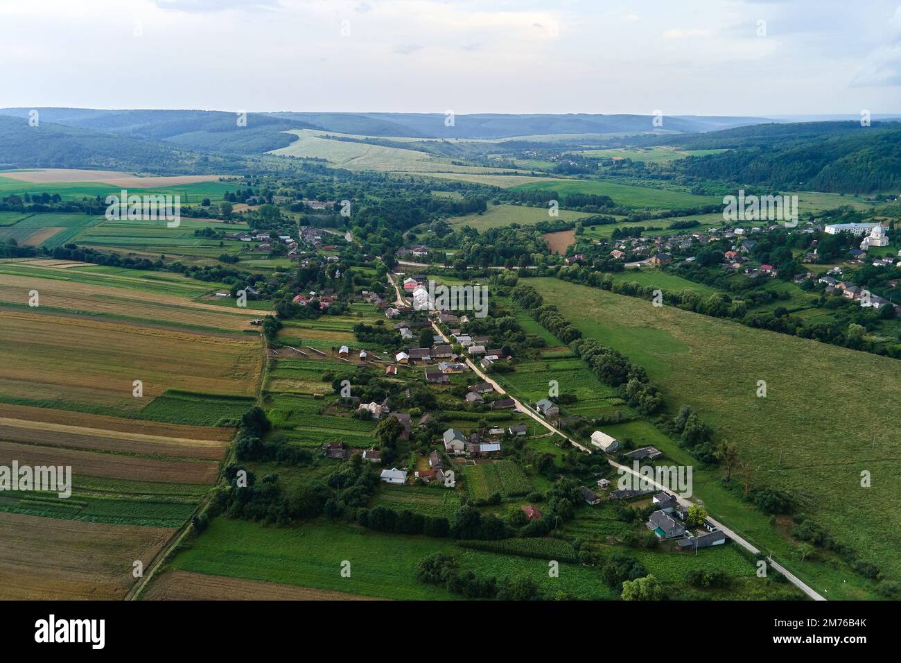 Veduta aerea del paesaggio di case di villaggio e campi agricoli coltivati a distanza verde con colture in crescita in luminoso giorno d'estate Foto Stock