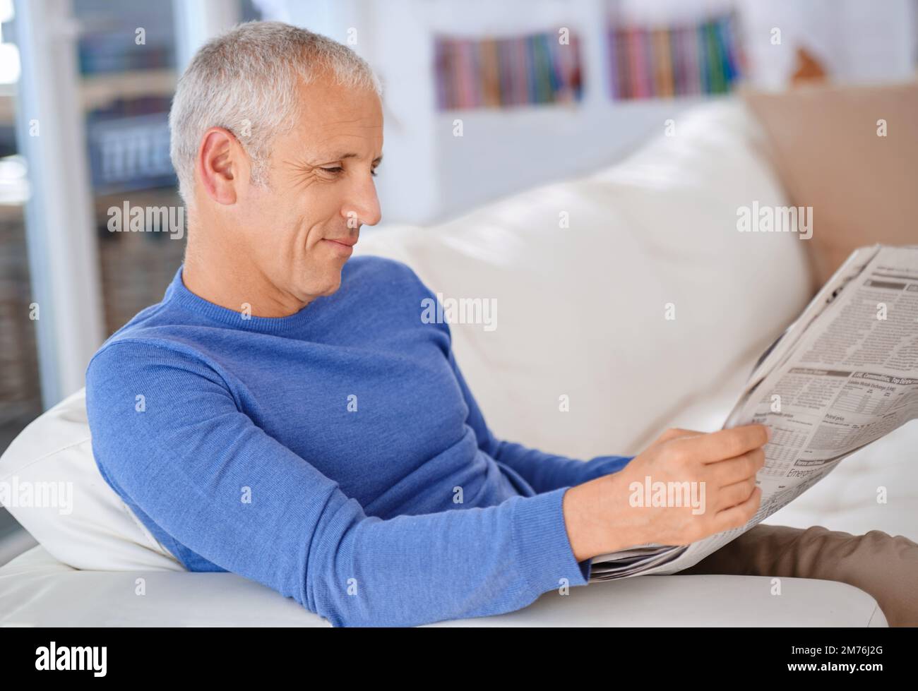 Godendo di una lettura interessante. un uomo maturo seduto sul divano del suo salotto che legge un giornale. Foto Stock