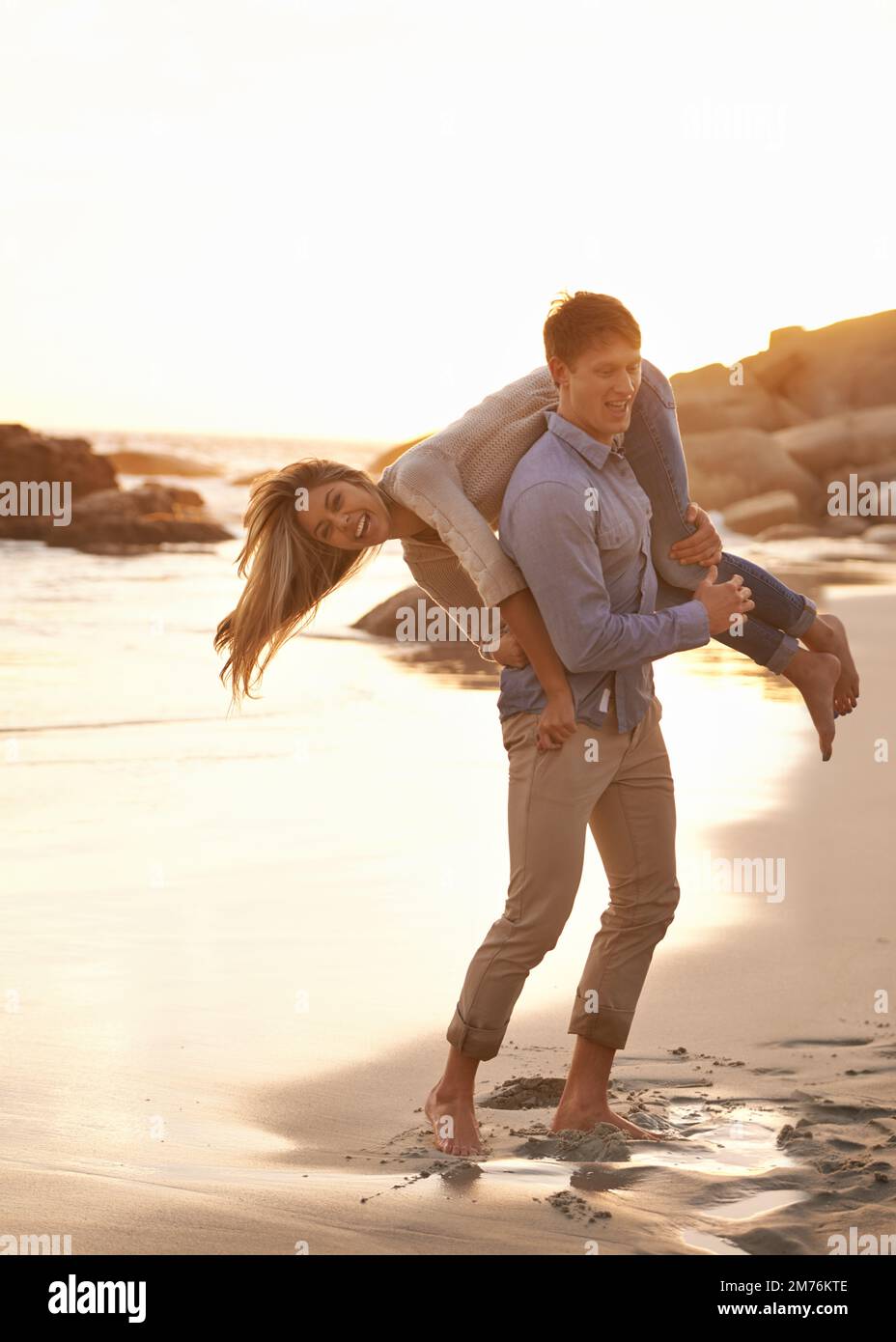 Partner in gioco. una giovane coppia felice che si diverte sulla spiaggia al tramonto. Foto Stock