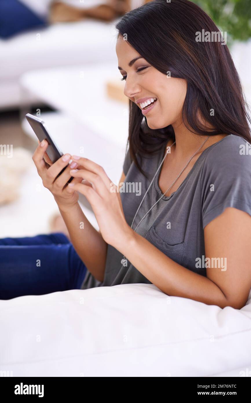 I suoi messaggi mi fanno sempre sorridere. una giovane donna attraente che usa il suo telefono cellulare a casa. Foto Stock