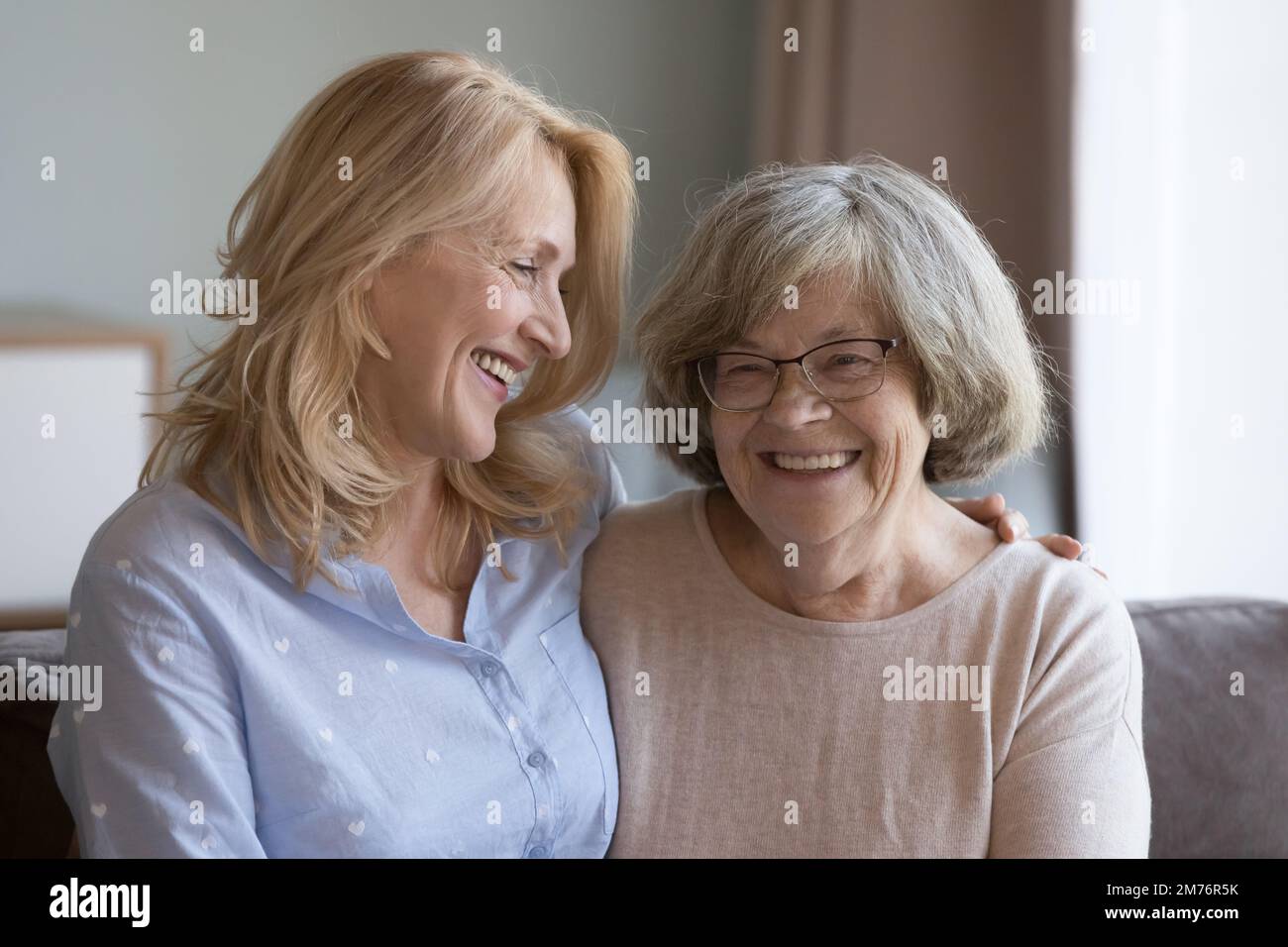 Giovane mamma gioiosa e donna figlia adulta che abbraccia il divano Foto Stock