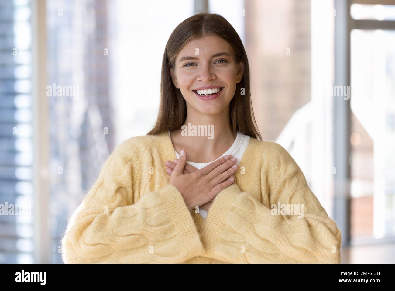 Una giovane donna grata ha messo palme piegate sul petto in posa interna Foto Stock