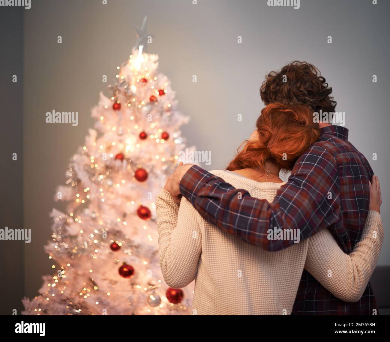 Il loro amore è più luminoso di tutte le luci su un albero di natale. Vista posteriore ripresa di una coppia che si lega al loro albero di Natale. Foto Stock