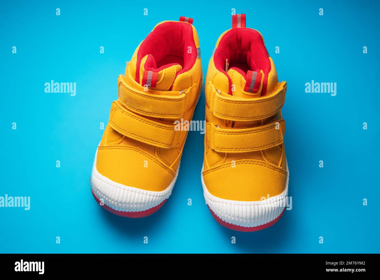 Scarpe per bambini gialle. Sneaker sportive per bambini isolate su sfondo blu Foto Stock