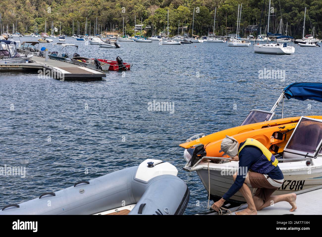 L'uomo assicura il suo piccolo motoscafo al molo dei pendolari di Church Point, Pittwater, Sydney, Australia utilizzando la corda intorno alla tacchetta Foto Stock