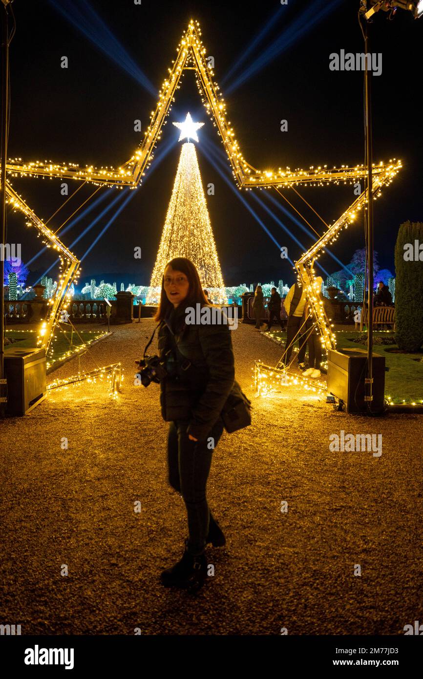 Donna che posa sotto l'esposizione illuminata delle stelle natalizie al Trentham Gardens Foto Stock