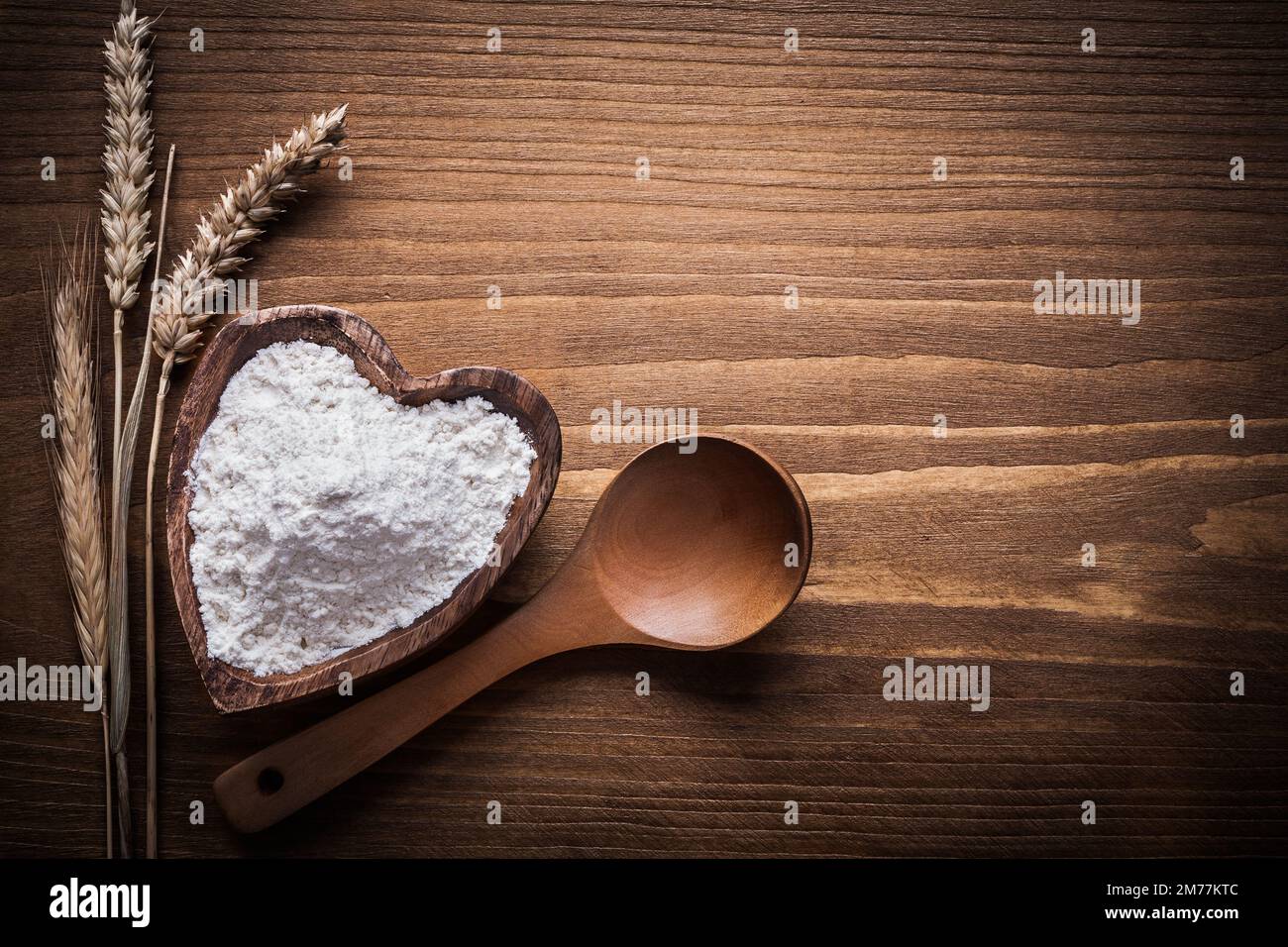 Cucchiaio di legno a forma di cuore ciotola fiore spighe di grano dorato. Foto Stock