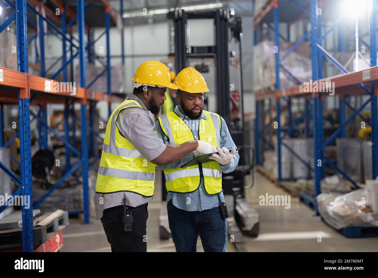 Afro-americano che lavora in magazzino tenere la lista di controllo delle scorte mentre camion caricare scatola di cartone vicino Foto Stock