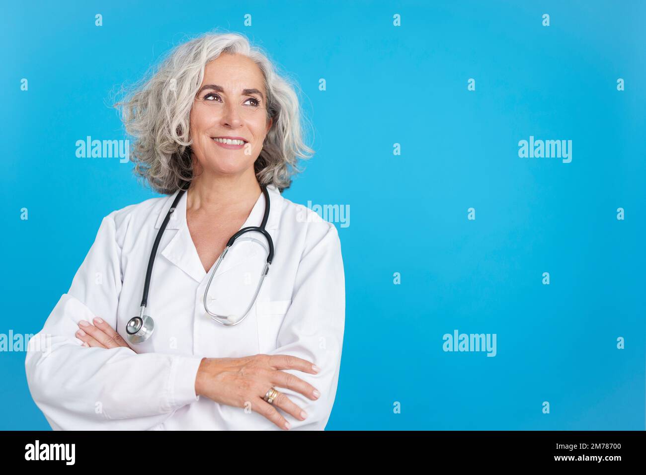 Maturo medico donna che guarda in su con le braccia incrociate Foto Stock
