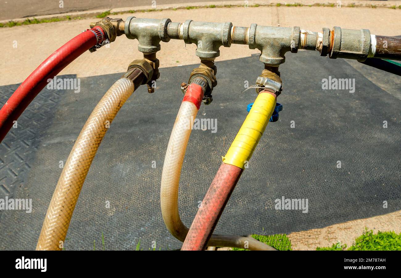 Tubi flessibili dell'acqua che alimentano da un tubo di metallo. Sono presenti quattro tubi flessibili. Uno sta gocciolando. Foto Stock