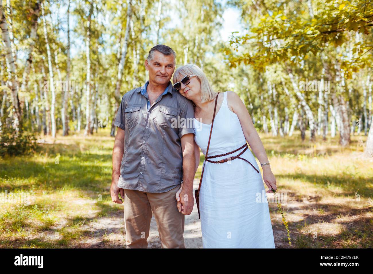 Ritratto di coppia di famiglia anziana che cammina all'aperto nella foresta estiva. Persone anziane che tengono le mani e abbracciano. Foto Stock