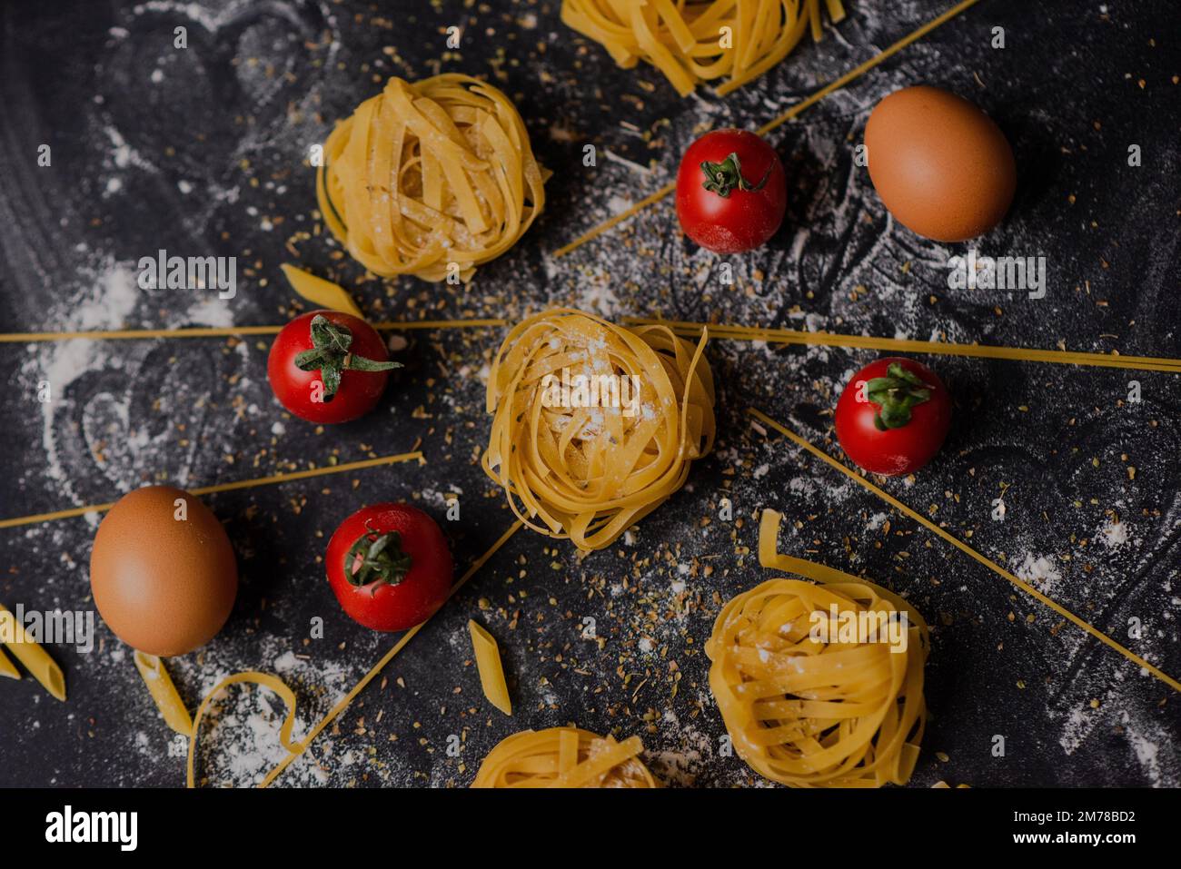 Un primo piano di pasta cruda preparata in un ambiente ben decorato con pomodori, sfondo nero Foto Stock