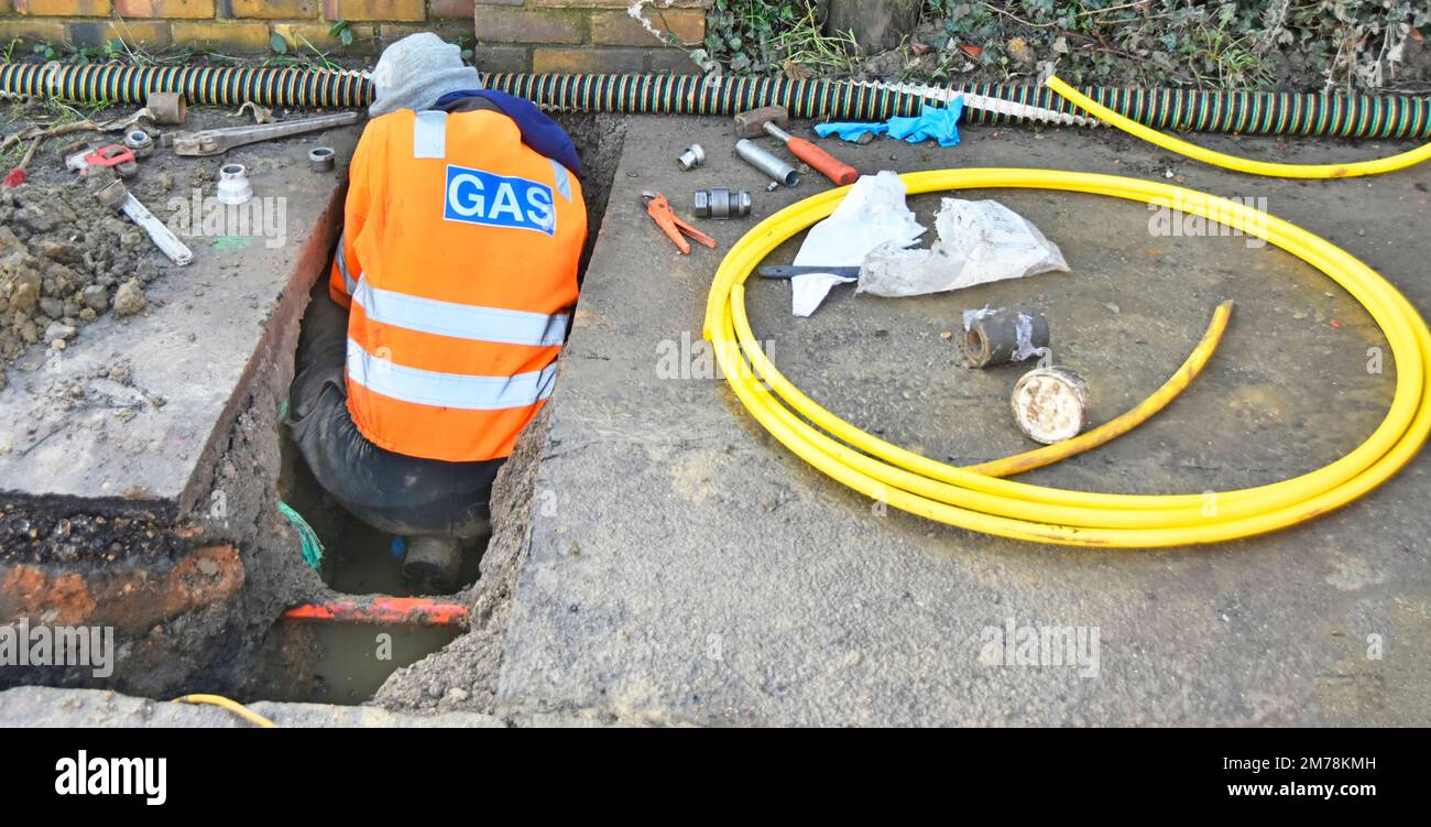 Gas principale lavoratore giù uno spazio limitato sporco in fossa waterlogged che collega il nuovo tubo giallo di plastica alla casa inserita in vecchi tubi di acciaio Inghilterra UK Foto Stock