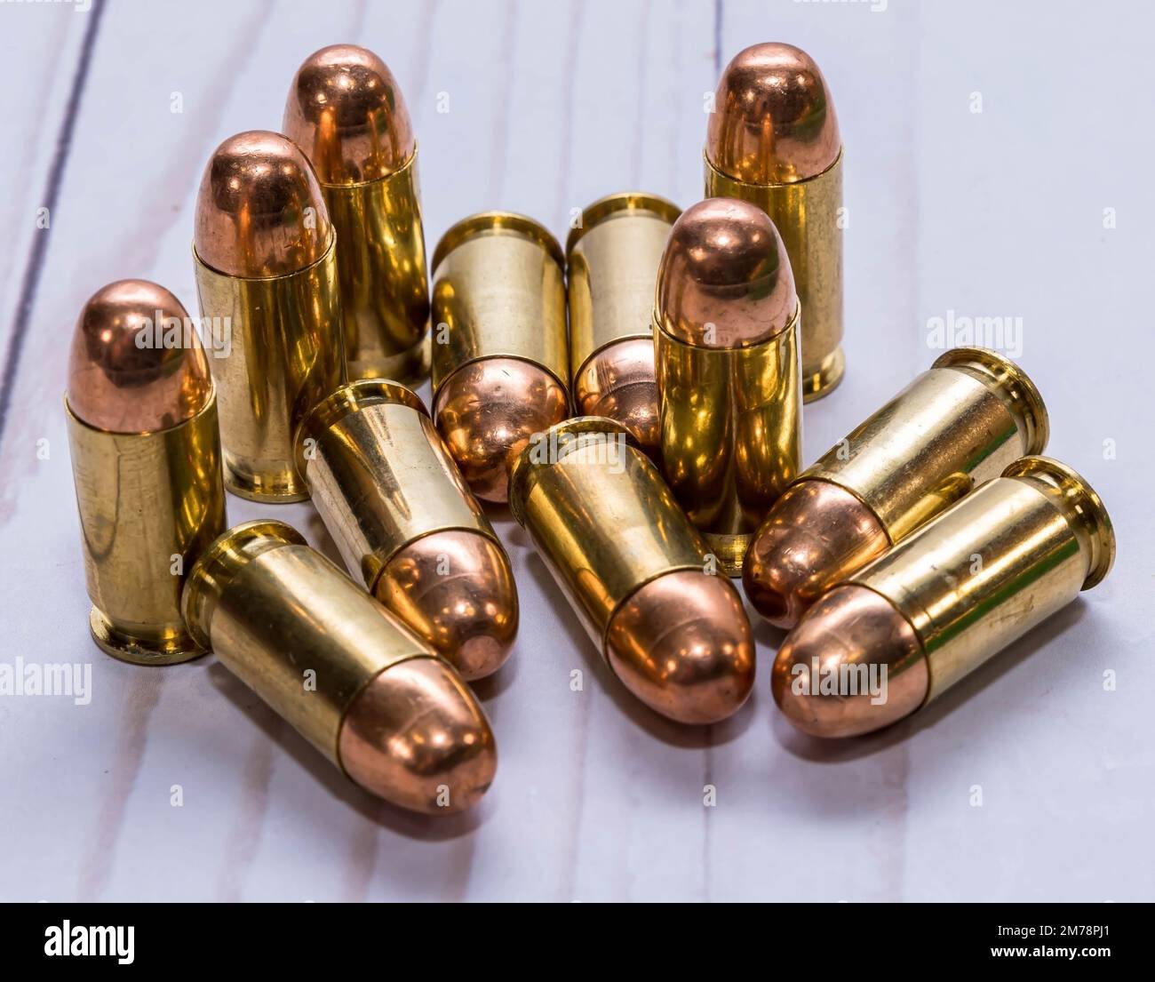 Dodici pallottole di metallo del calibro di 45acp su uno sfondo di legno bianco Foto Stock