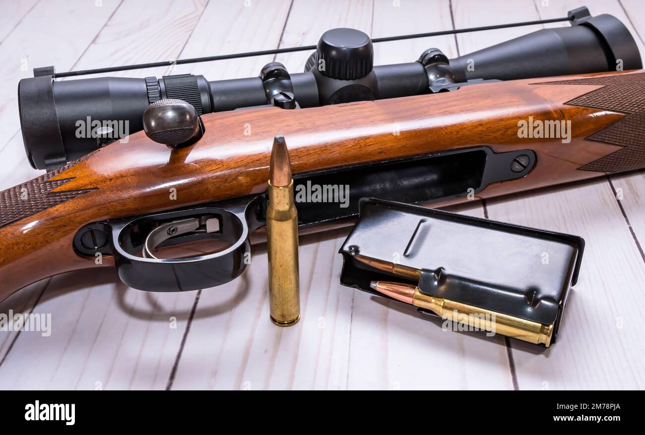 Un fucile da caccia in legno di calibro 30,06 con un caricatore caricato accanto ad esso su uno sfondo di legno bianco Foto Stock