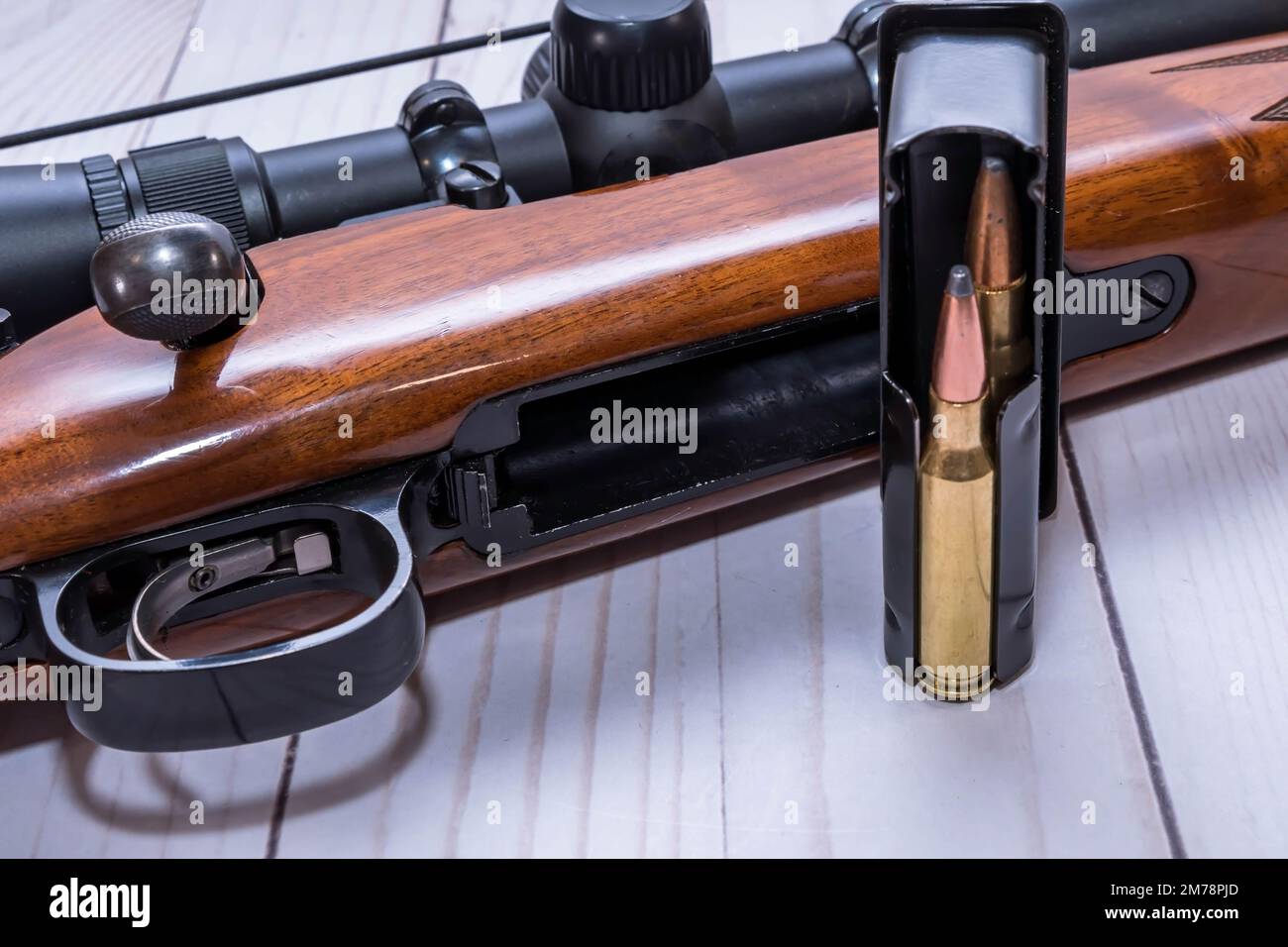 Un fucile da caccia in legno di calibro 30,06 con un caricatore caricato accanto ad esso su uno sfondo di legno bianco Foto Stock