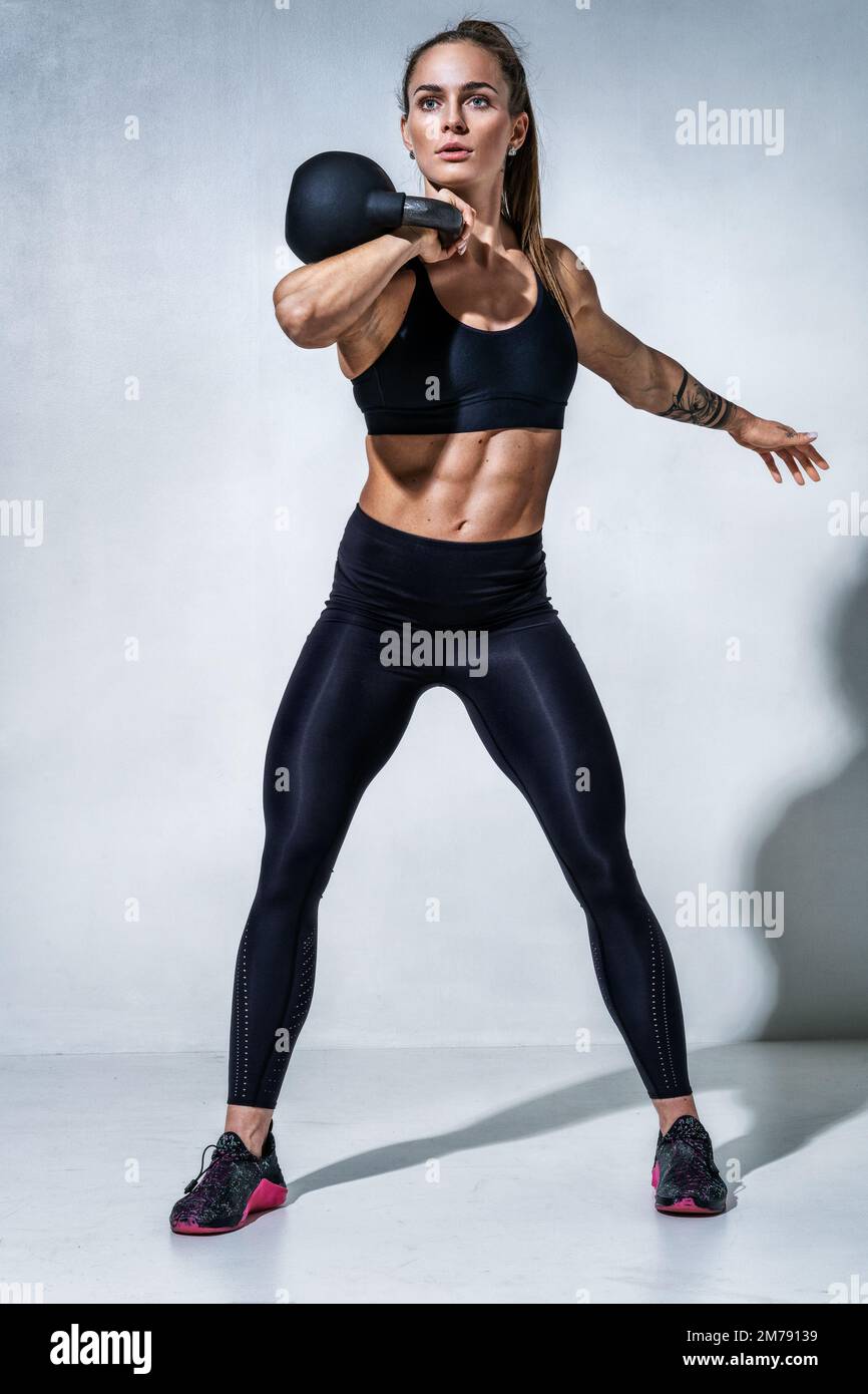 Allenamento sportivo femminile con Kettlebell. Foto di donna in abbigliamento sportivo nero su sfondo grigio. Motivazione sportiva e stile di vita sano Foto Stock