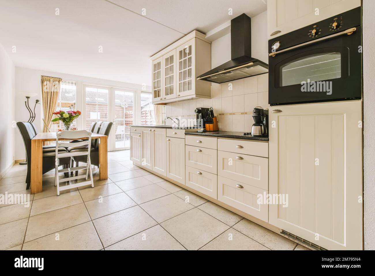 una cucina con armadi bianchi e elettrodomestici neri sui ripiani, insieme  con una zona pranzo sullo sfondo Foto stock - Alamy