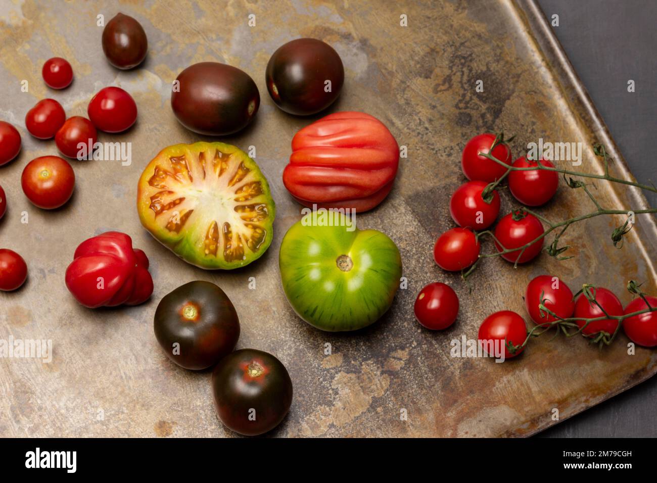 Pomodori verdi, marroni e rossi. Ramo di pomodoro ciliegia. Giacitura piatta. Fondo in metallo arrugginito. Foto Stock