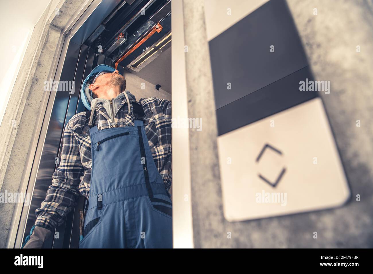 Tecnico dell'ascensore caucasico professionista che fissa le porte dell'ascensore in un edificio residenziale di nuova costruzione. Manutenzione della macchina di sollevamento. Foto Stock