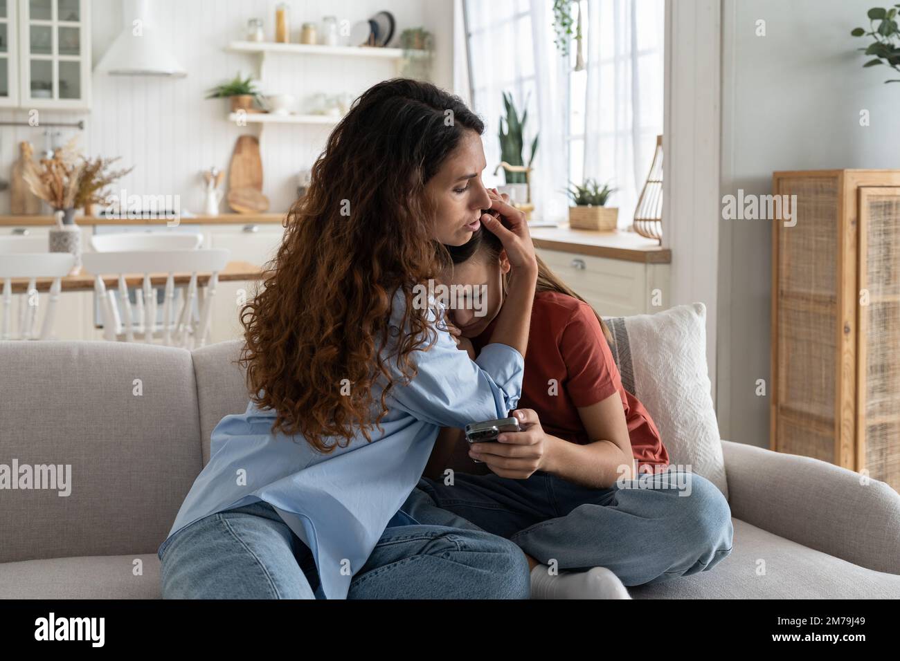 Cura gentile donna hugging sconvolto piangendo ragazza teen siede sul divano con telefono e soffre di stress Foto Stock