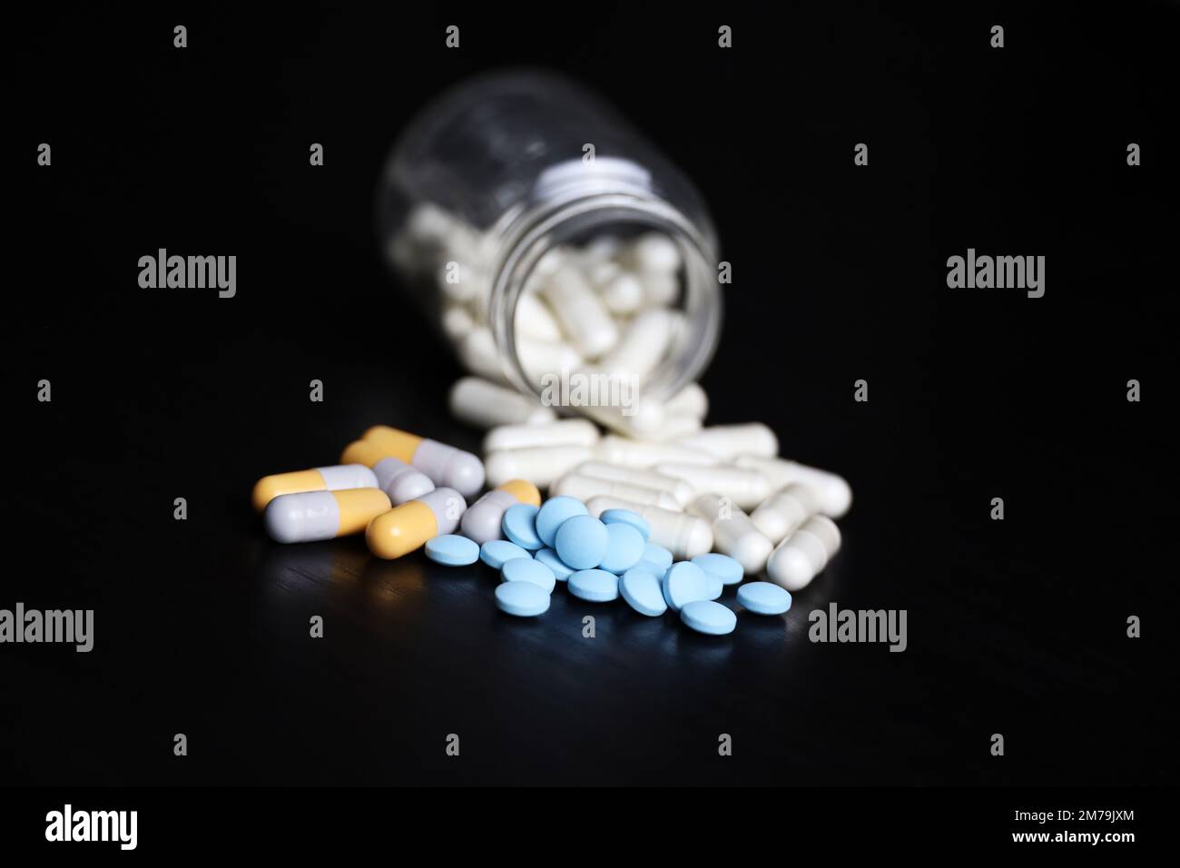 Pillole su un tavolo di legno nero, variazione del farmaco in capsule sparse da una bottiglia. Background per farmacia, antibiotici, vitamine Foto Stock