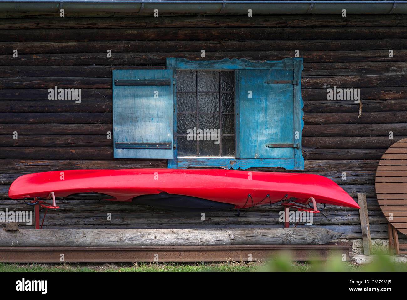 Kayak rosso sospeso da una capanna di legno con persiane blu, Baviera, Germania Foto Stock