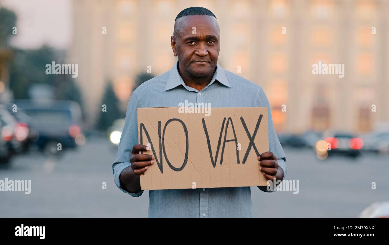 Concetto di fobia della vaccinazione delle persone. L'uomo afroamericano anziano adulto si leva in piedi nella strada della città tenendo la bandiera del segno con il testo Nessun VAX nella protesta di Foto Stock