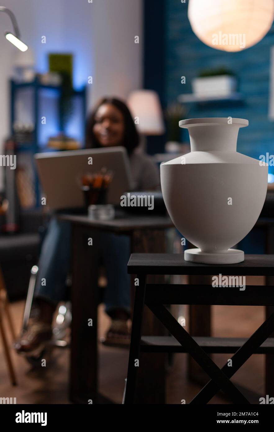 Donna con capacità artistiche che utilizza la sedia a rotelle per spostarsi, rivedendo le tecniche di disegno online dal computer portatile in casa studio d'arte. afroamericano che crea vasi di grafica digitale su computer. Foto Stock