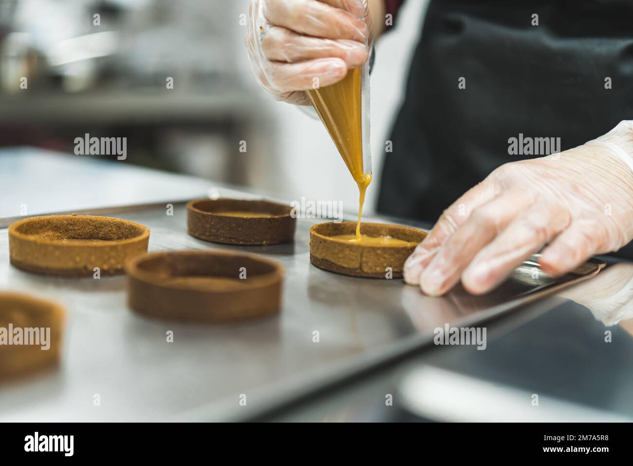 Primo piano di un esperto con guanti trasparenti che mettono il caramello su una crostata. Foto di alta qualità Foto Stock