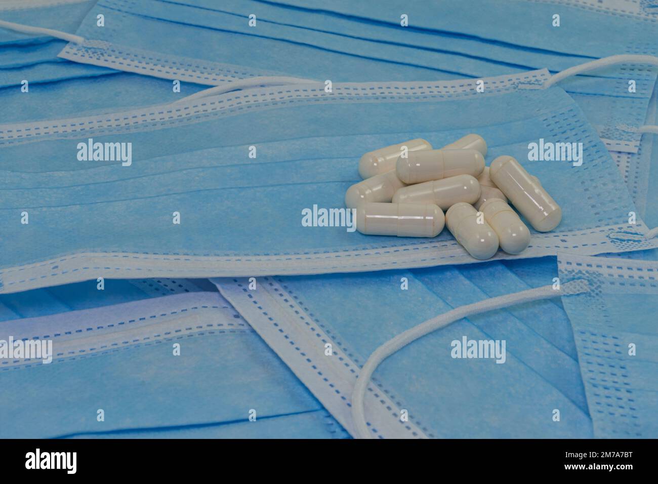 Un mucchio di pillole bianche si trova su maschere mediche blu (primo piano). Medicina moderna. Trattamento delle malattie. Nessun covid Foto Stock