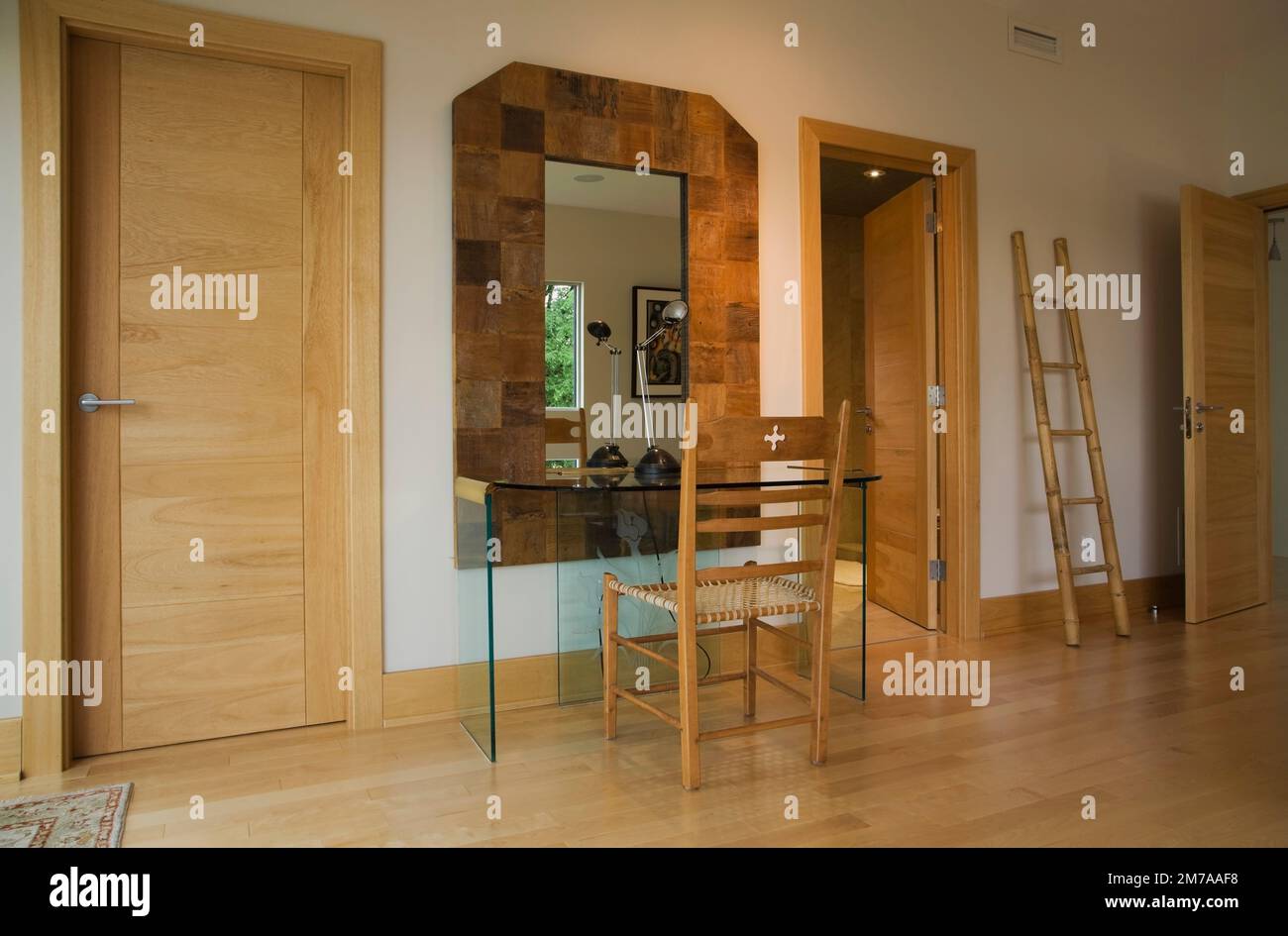 Scrivania in vetro e antico sedile in tessuto rawhide con schienale alto in legno e scala decorativa nella camera da letto principale all'interno di una casa moderna in stile cubista. Foto Stock